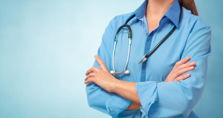 Female doctor in lab coat with arms crossed on blue background. Copy space