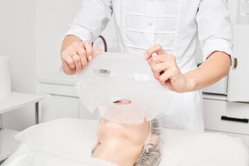 Cosmetologist applying sheet mask on woman face for rehydrate face skin, revitalize cosmetic...