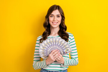 Photo portrait of lovely young lady holding money fan rich successful dressed stylish striped clothes isolated on yellow color background