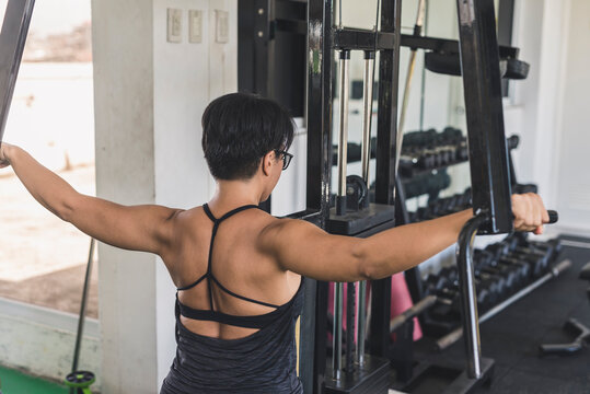 A short haired asian woman does a set of reverse pec deck flys at the gym. Focusing on the posterior deltoids and upper back muscles.