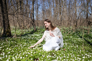 Woman in the forest. A girl in white among white flowers. The girl admires the beauty of flowers. Charming mood, tenderness, cleanliness