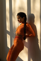 Beautiful young woman with natural make-up, dressed in a orange sports uniform, posing in the studio on a white wall.Advertising sportswear and yoga wear. Healthy lifestyle, sport