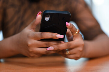 Beautiful hands of a smart African American lady using her smartphones whilst sitting inclined to a brown bar table 