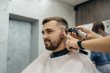 A close-up photo of a man's hair cut. A professional hairdresser cuts a man with beard in a barbershop. Men's beauty salon.