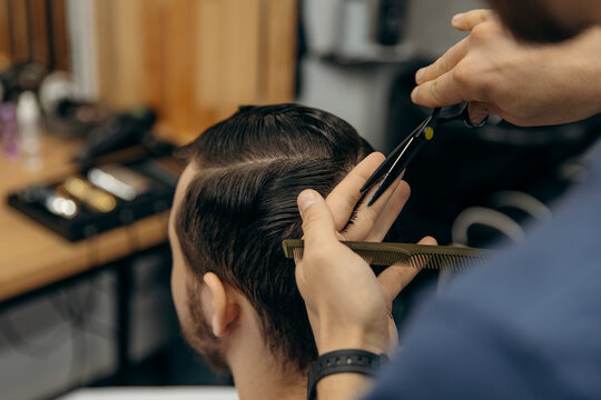 A close-up photo of a man's hair cut. A professional hairdresser cuts a man with scissors in a barbershop. Men's beauty salon.