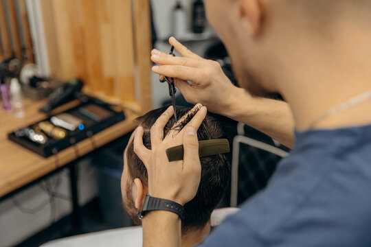 A professional hairdresser cuts a man with scissors in a barbershop. Men's beauty salon. Hair leveling.