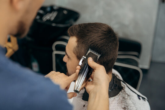 A close-up photo of a man's hair cut. A professional hairdresser cuts a man head in a barbershop. Men's beauty salon.