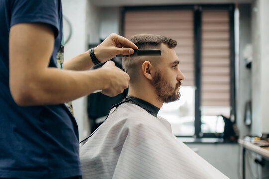 A close-up photo of a man's hair cut. A professional hairdresser cuts a man with beard in a barbershop. Men's beauty salon.