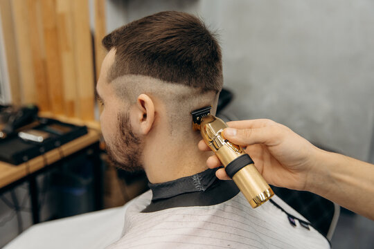 A close-up photo of the men's haircut process. A professional hairdresser cuts a man's hair with a golden clipper in a barbershop. Men's beauty salon.