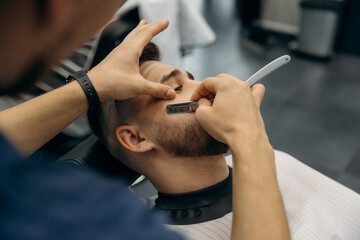 The process of trimming a man's beard with a dangerous razor. A barber cuts a beard in a barbershop. Beard trimming in a beauty salon for men