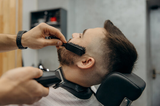 A close-up photo of a man's beard haircut. A barber cuts a beard in a barbershop. Beard trimming in a beauty salon for men
