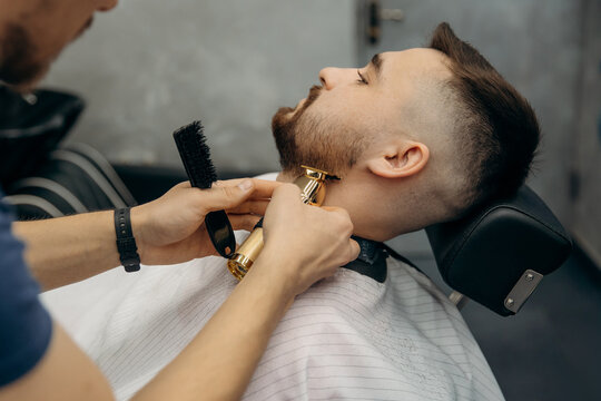 The process of trimming a man's beard with a gold clipper. A barber cuts a beard in a barbershop. Beard trimming in a beauty salon for men