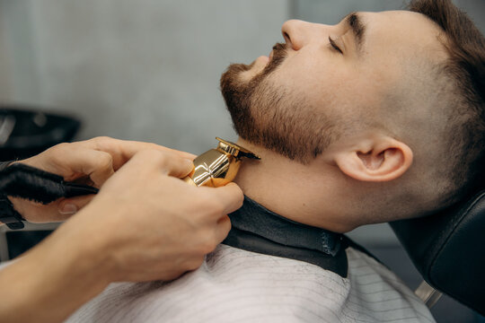 The process of trimming a man's beard with a gold clipper. A barber cuts a beard in a barbershop. Beard trimming in a beauty salon for men
