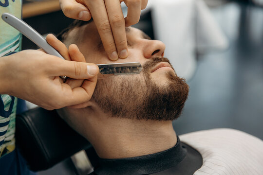 close up photo  of trimming a man's beard with a dangerous razor. A barber cuts a beard in a barbershop. Beard trimming in a beauty salon for men