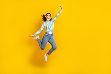 Full length photo of adorable lovely positive girl wear striped shirt denim pants flying like plane isolated on yellow color background