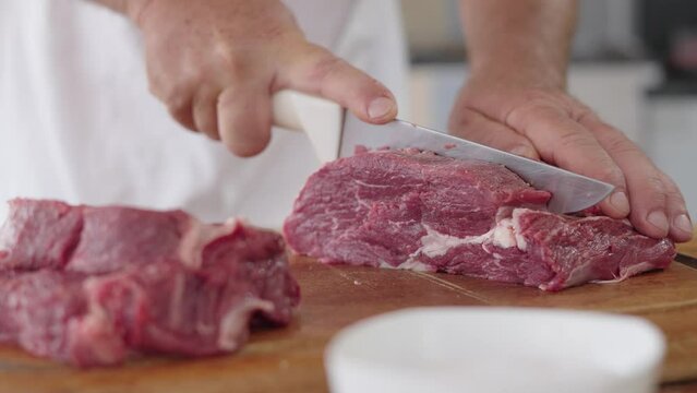 Butcher cuts carcass of ancho meat. Action. Close-up of professional knife cutting huge piece of ancho meat in butcher shop
