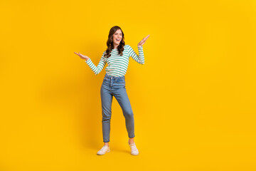 Full length photo of cute girl wavy hairdo dressed striped shirt raising palms dancing have fun isolated on yellow color background