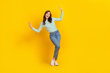 Fototapeta na wymiar Full length photo of pleasant girl wavy hairdo dressed striped shirt raising palms dancing having fun isolated on yellow color background