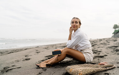 Smiling woman resting on sandy beach with smartphone