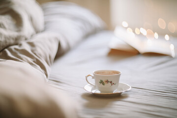 Fototapeta na wymiar Light cozy bedroom, Coffee or tea cup and an open book on the bed. Spring still life. Breakfast in bed.