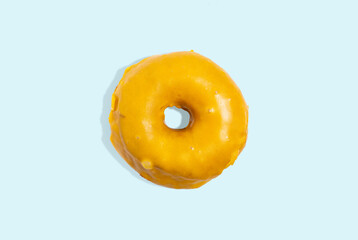 Obraz na płótnie Canvas Delicious traditional donut with yellow glaze isolated on blue background. Modern food concept. Advertising for pastry shops, cafes.
