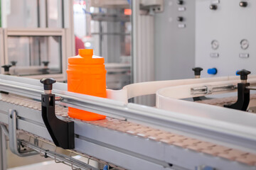 Empty orange plastic jerrycan moving on conveyor belt of automatic pet blow molding machine at...