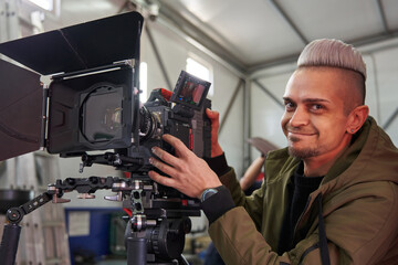 young caucasian man videographer smiling next to a professional movie camera