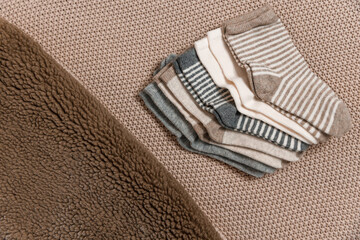 Children's socks in beige and gray colors lie on a beige plaid, decorated with fur, top view