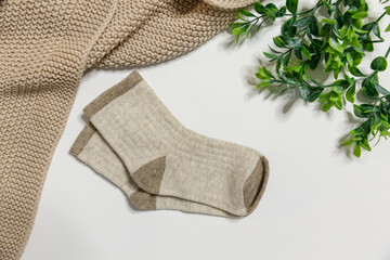 Brown children's socks, for newborn boys or girls on a light background. Decorated with a beige plaid and greenery top view. For shops and manufacturers of children's clothingchildren's socks