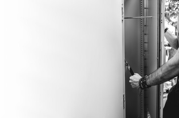 Fit young latino worker opening a steel door of a electronic area (panoramic with big copy space in black and white)