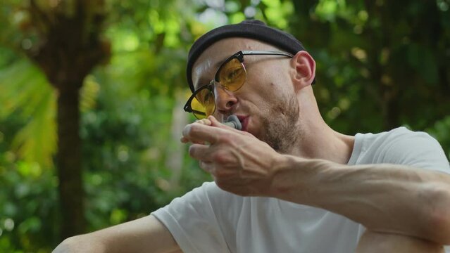 Stoned man smokes weed and smiles looking at camera. Male stoner smoking cannabis using pipe, portrait. Close up of marijuana smoker