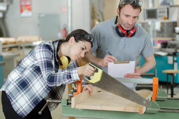 female carpenter cutting plank with hand saw