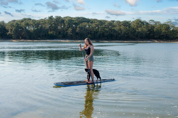 Fototapeta na wymiar Beautiful young woman stand up paddling with her Border Collie puppy
