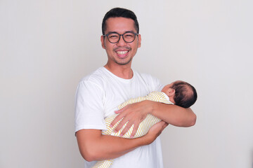 Asian father smiling happy at the camera while holding his newborn baby