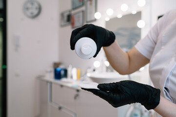 Crop cosmetologist pouring product on cotton pad for facial skin care © BullRun