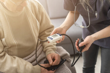 Smiling young nurse taking old man's blood pressure