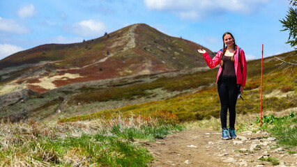 Beautiful fit happy girl in pink jacket enjoys hike in stunning colorful mountain scenery. Spring in the Bieszczady Mountains, Poland, Europe