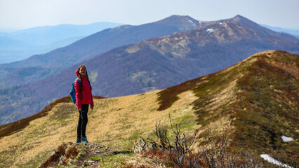 Fototapeta premium Beautiful fit happy girl in pink jacket enjoys hike in stunning colorful mountain scenery. Spring in the Bieszczady Mountains, Poland, Europe