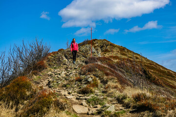 Beautiful fit happy girl in pink jacket enjoys hike in stunning colorful mountain scenery. Spring in the Bieszczady Mountains, Poland, Europe