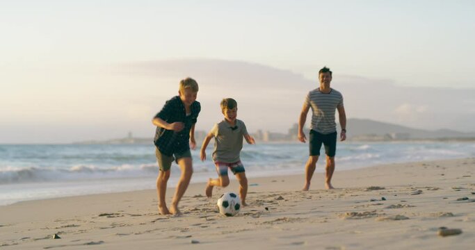 Father, son and brother playing with a soccer ball on the beach and bonding as a family by the sea. Kicking, playing and having fun with young children and their dad on summer vacation or holiday