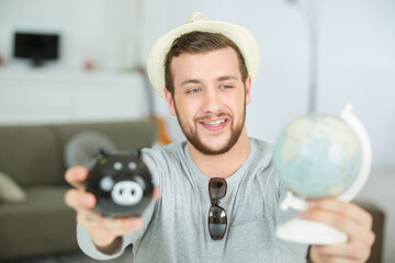 man showing a world-globe and a piggy bank