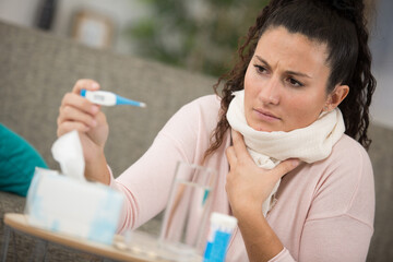 ill woman is checking a thermometer at home