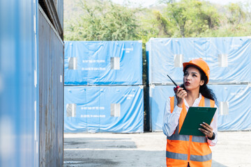 Smiling portrait of beautiful asian female industrial engineer wearing white helmet, vest holding walkie talkie. Safety Supervisor at Container Terminal
