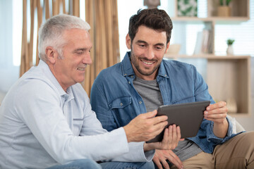 two men sit comfortably at home looking at a tablet