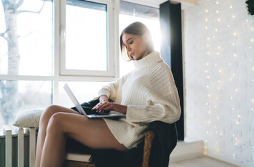 Focused woman sitting on armchair and working on laptop