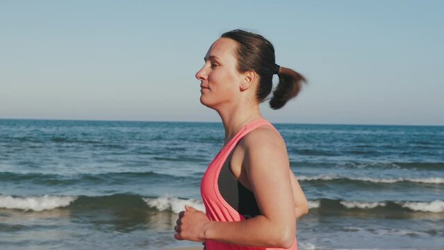 Motivated woman running along seashore in morning.Female runner jogging on beach