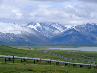 Fresh July snowfall on the mountains of the Brooks Range with the Alaska Oil Pipeline in the foreground traversing miles of empty Tundra