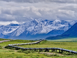 Beautiful rugged and snow-covered Mountain peaks of the Brooks Range in Alaska between the Coldfoot Camp and Prudhoe Bay with the Alaska Oil Pipeline traversing the treeless Tundra - 574705791