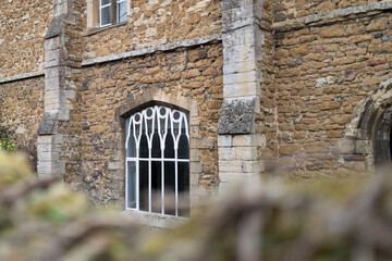 Shallow focus of a wrought iron and painted gothic window frame seen over a blurred garden wall.