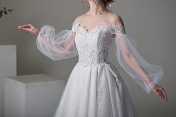 A beautiful young bride model in long lace dress in minimalist white studio interior. Wedding photography.